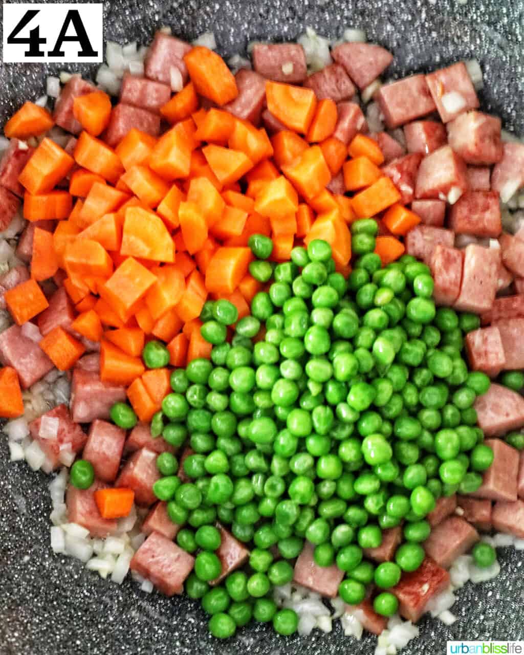 cooking cubed spam, garlic, onions, peas, and carrots in a wok.