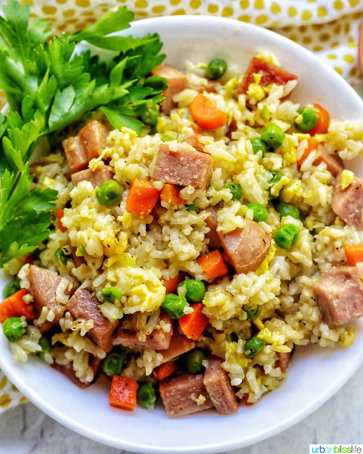 spam fried rice with peas, carrots, and parsley garnish in a white bowl.