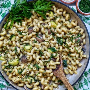 zucchini mushroom pasta in a large saucepan next to small bowls of grated parmesan cheese and chopped parsley.