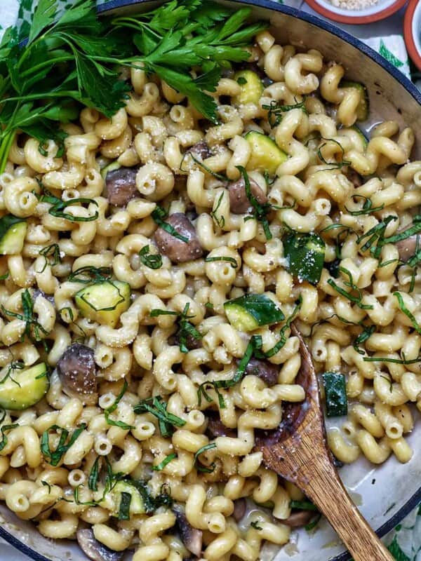 zucchini mushroom pasta in a large saucepan next to small bowls of grated parmesan cheese and chopped parsley.