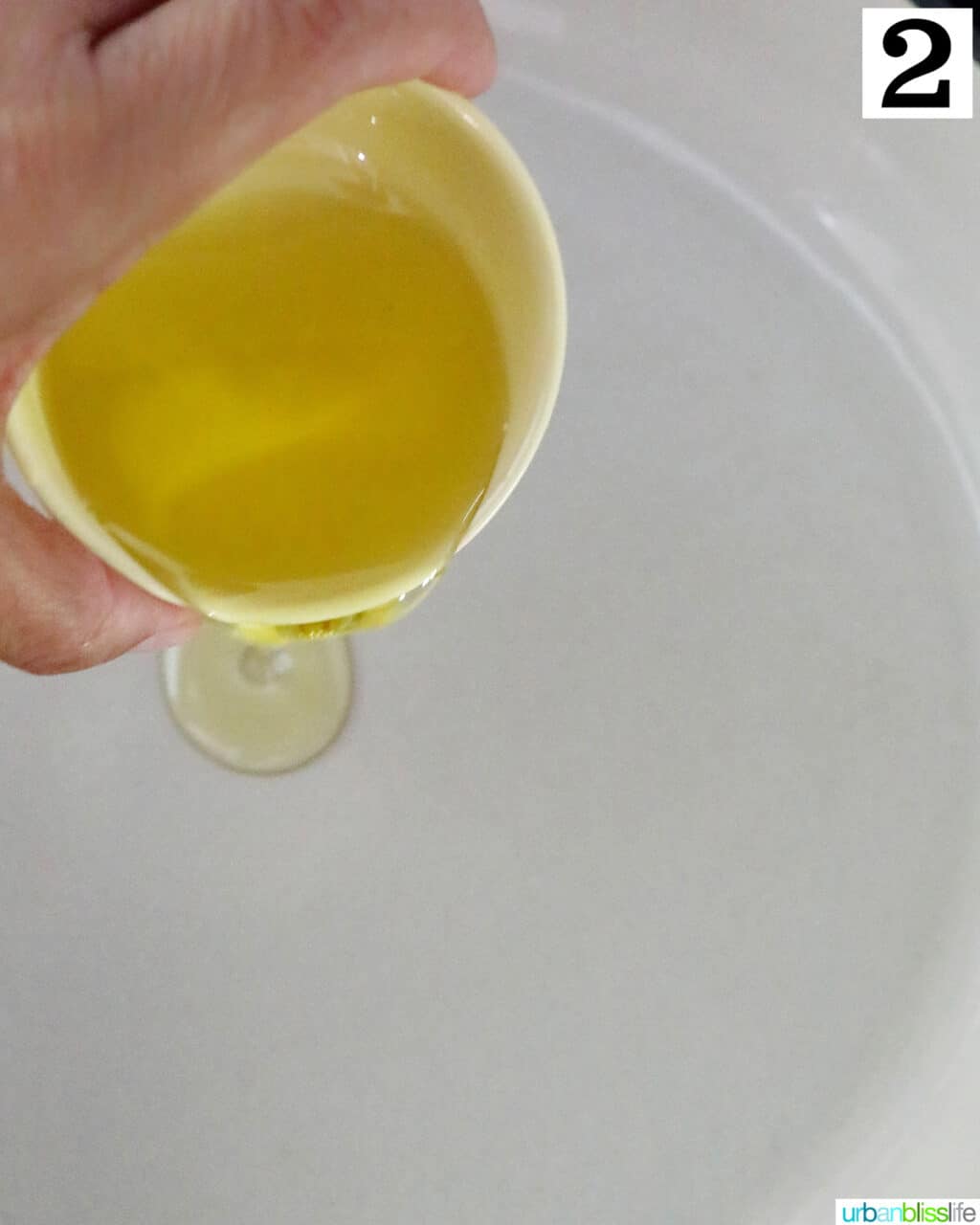 hand pouring olive oil into a white saucepan.