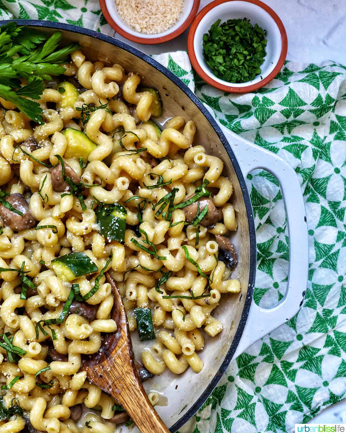 zucchini mushroom pasta in a large saucepan next to small bowls of grated parmesan cheese and chopped parsley.