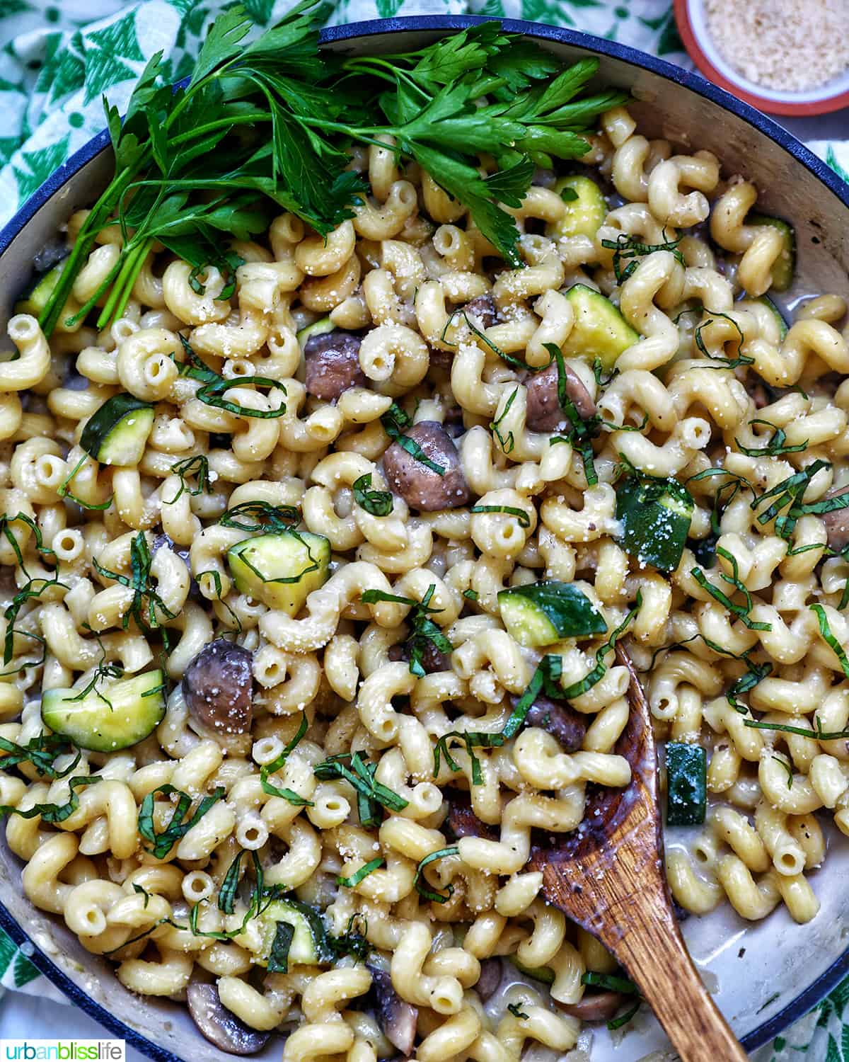 zucchini mushroom pasta in a large saucepan next to small bowls of grated parmesan cheese and chopped parsley.