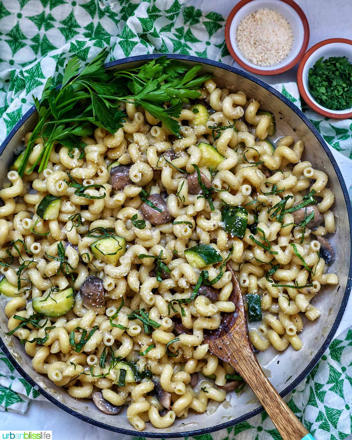 zucchini mushroom pasta in a large saucepan next to small bowls of grated parmesan cheese and chopped parsley.