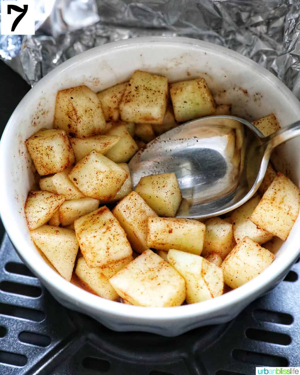 white bowl with spiced apples and a spoon in an air fryer basket.
