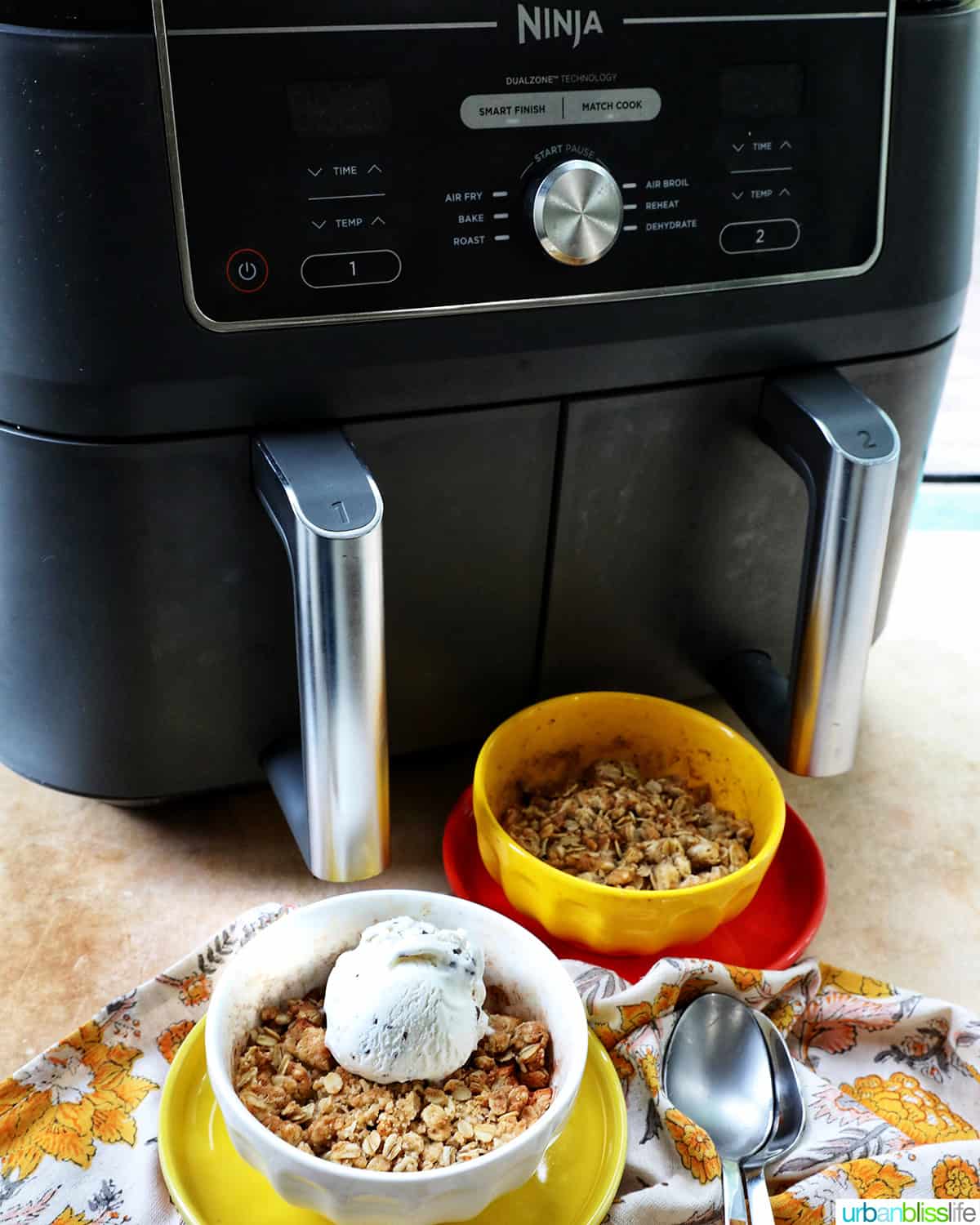 Ninja Air Fryer with two bowls of Air Fryer Apple Crisp and spoons.