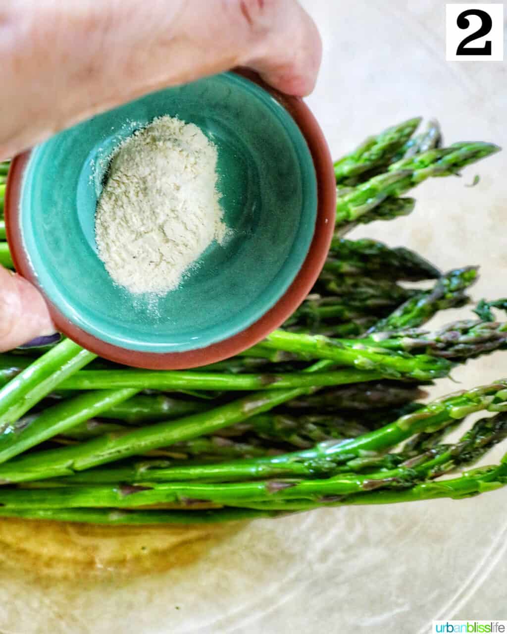 hand holding a bowl of garlic powder over asparagus.