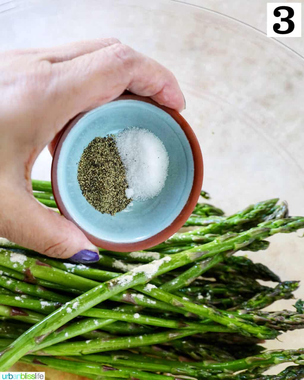 hand holding salt and pepper over asparagus.