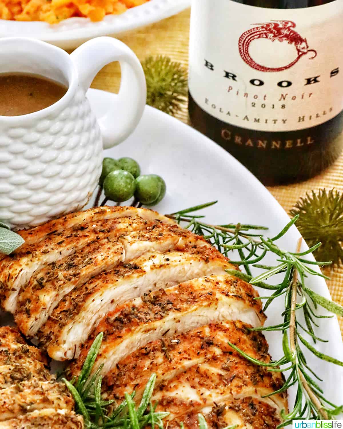 sliced turkey breast on a plate with fresh herbs and lemon slices and gravy and bottle of wine.