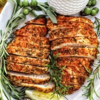 two sliced turkey tenderloins on a plate with fresh herbs and lemon slices.