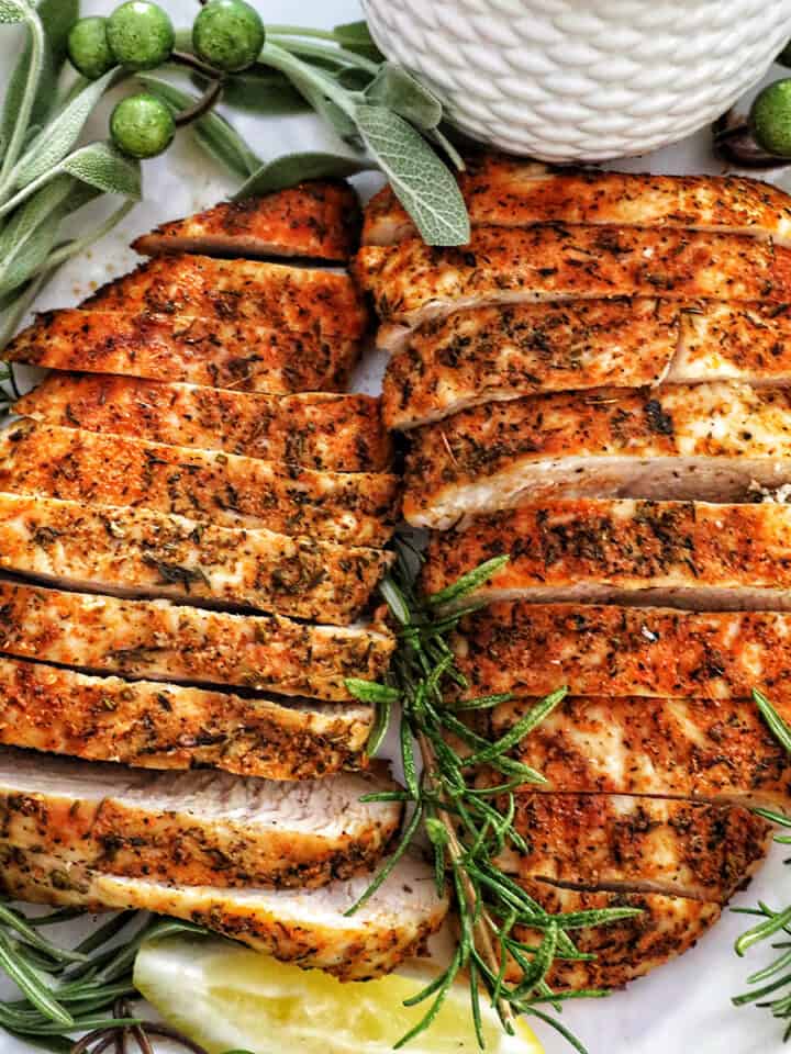 two sliced turkey tenderloins on a plate with fresh herbs and lemon slices.