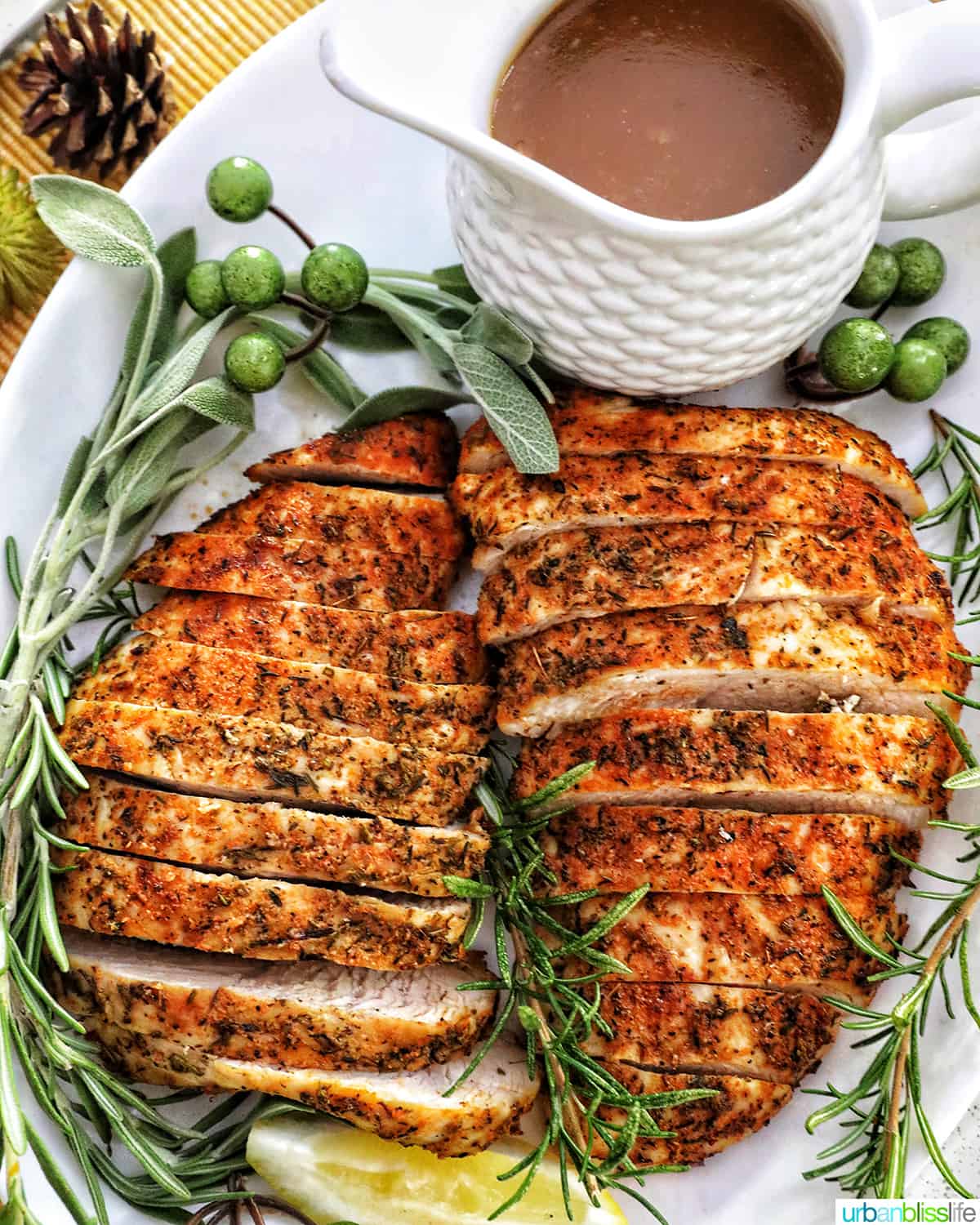 two sliced turkey tenderloins on a plate with fresh herbs and lemon slices and gravy.