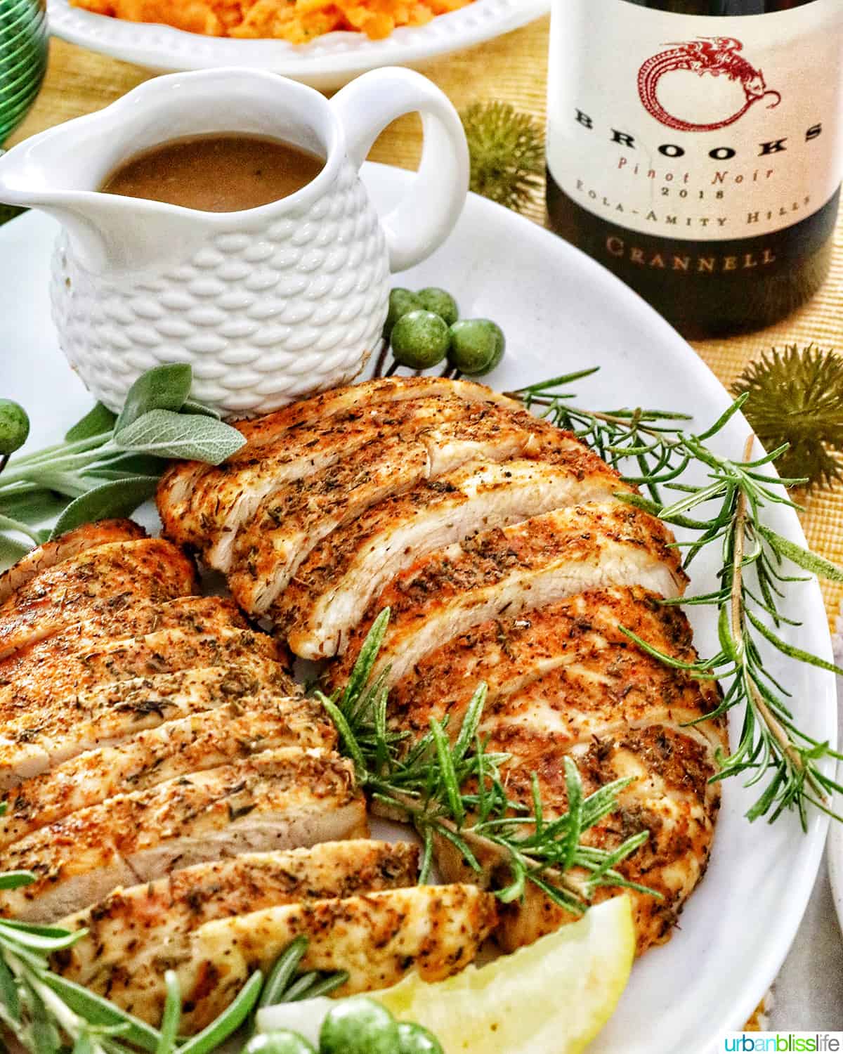 plate of sliced turkey tenderloin with sides of gravy and sweet potatoes and a bottle of wine.