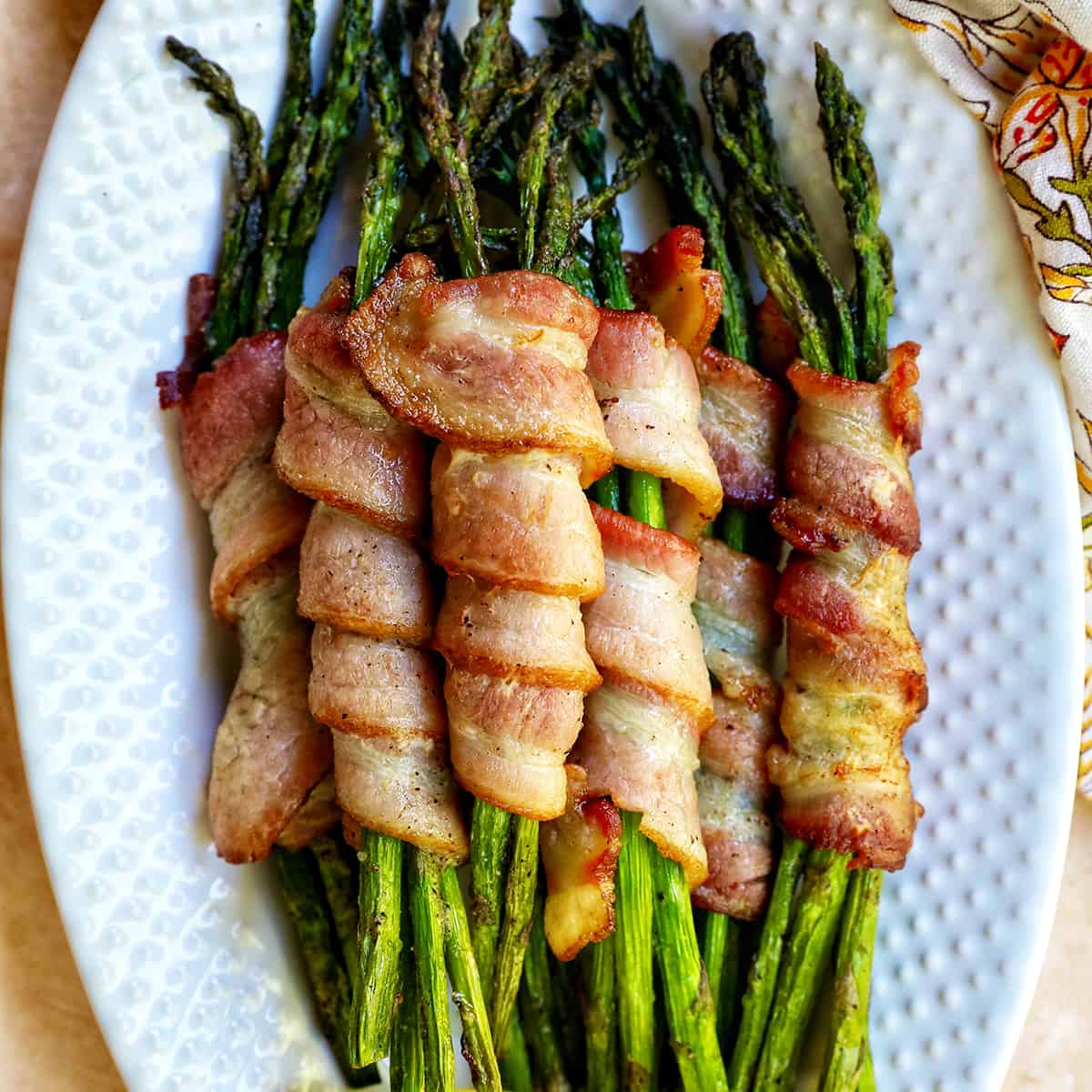bacon wrapped asparagus on a white plate.