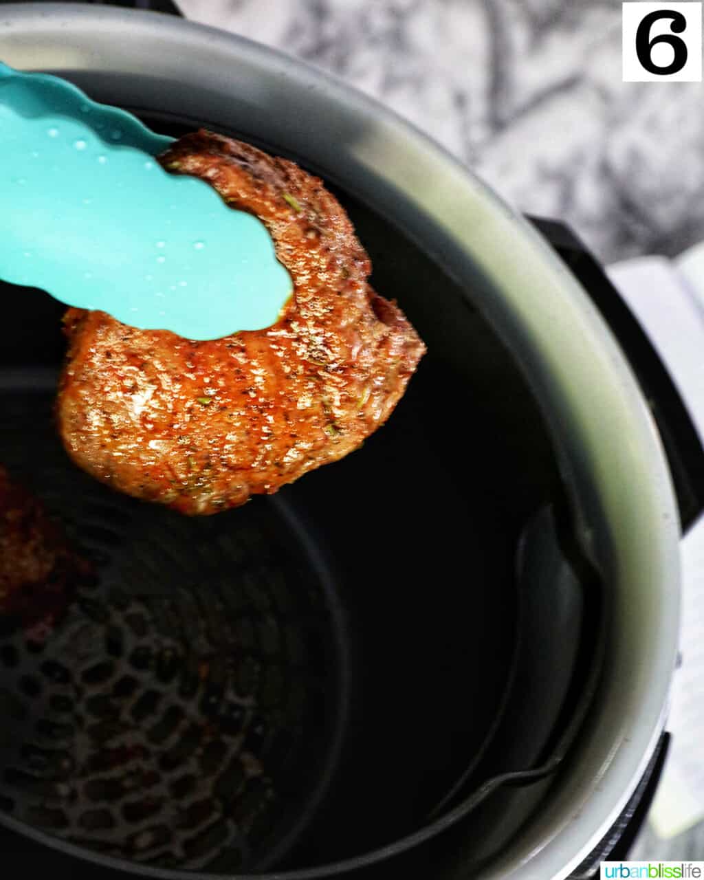 blue tongs holding up a half-cooked filet mignon over an air fryer.