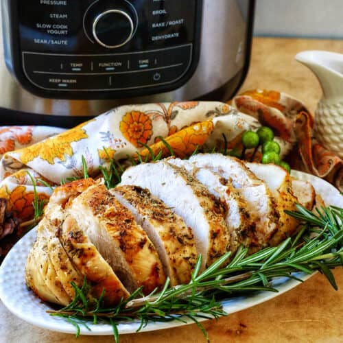 sliced turkey breast on a plate with herbs in front of an air fryer.