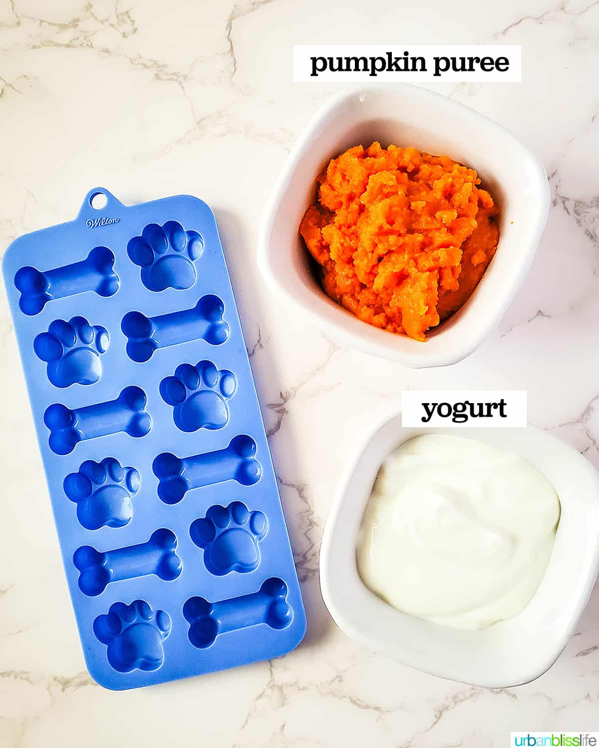 dog treats silicone mold next to a bowl of pumpkin puree and a bowl of yogurt.