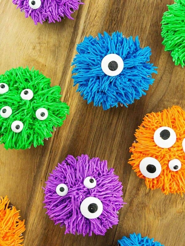 several colorful bright halloween monster cupcakes on a wood board.