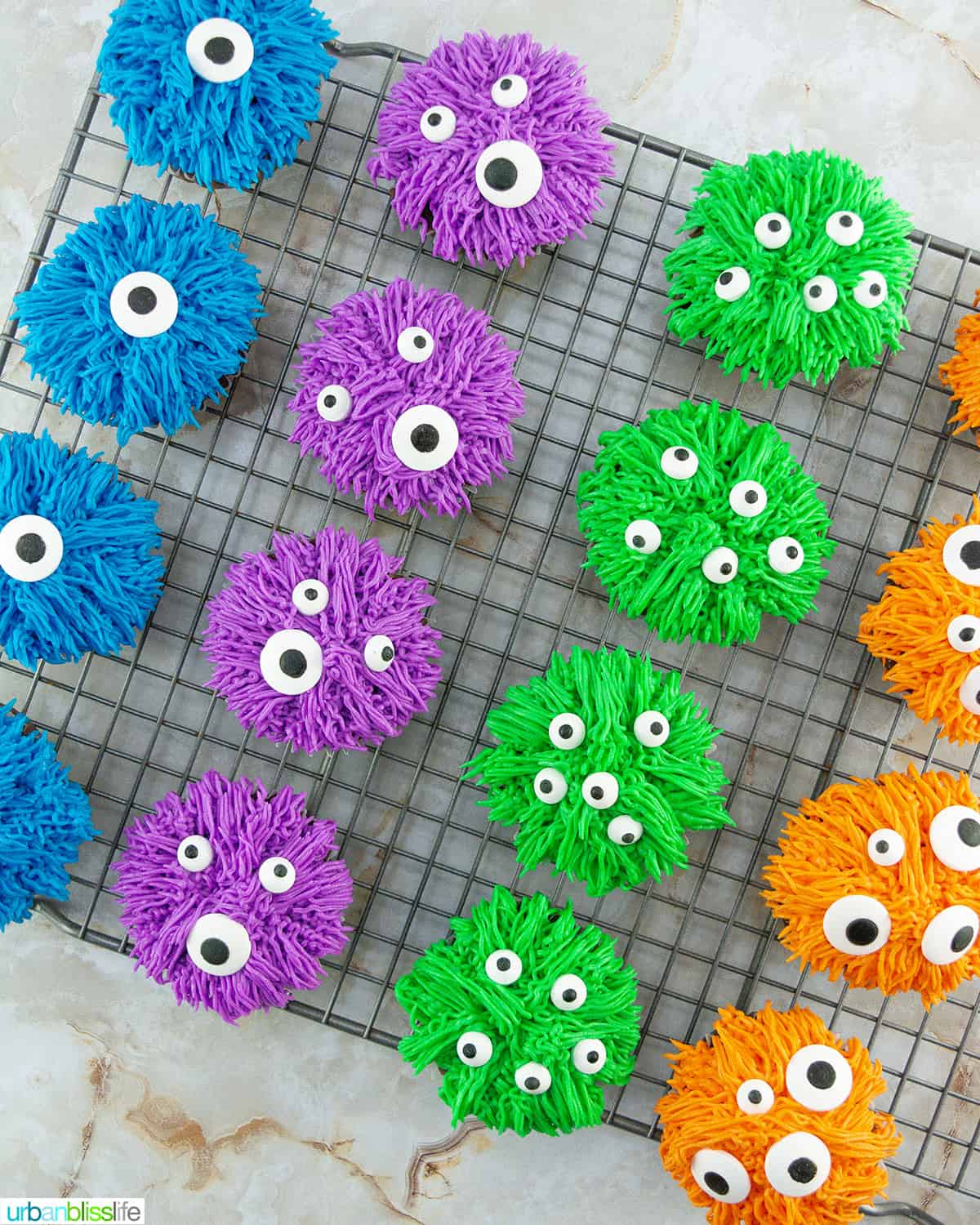 several colorful bright halloween monster cupcakes on a wire rack.