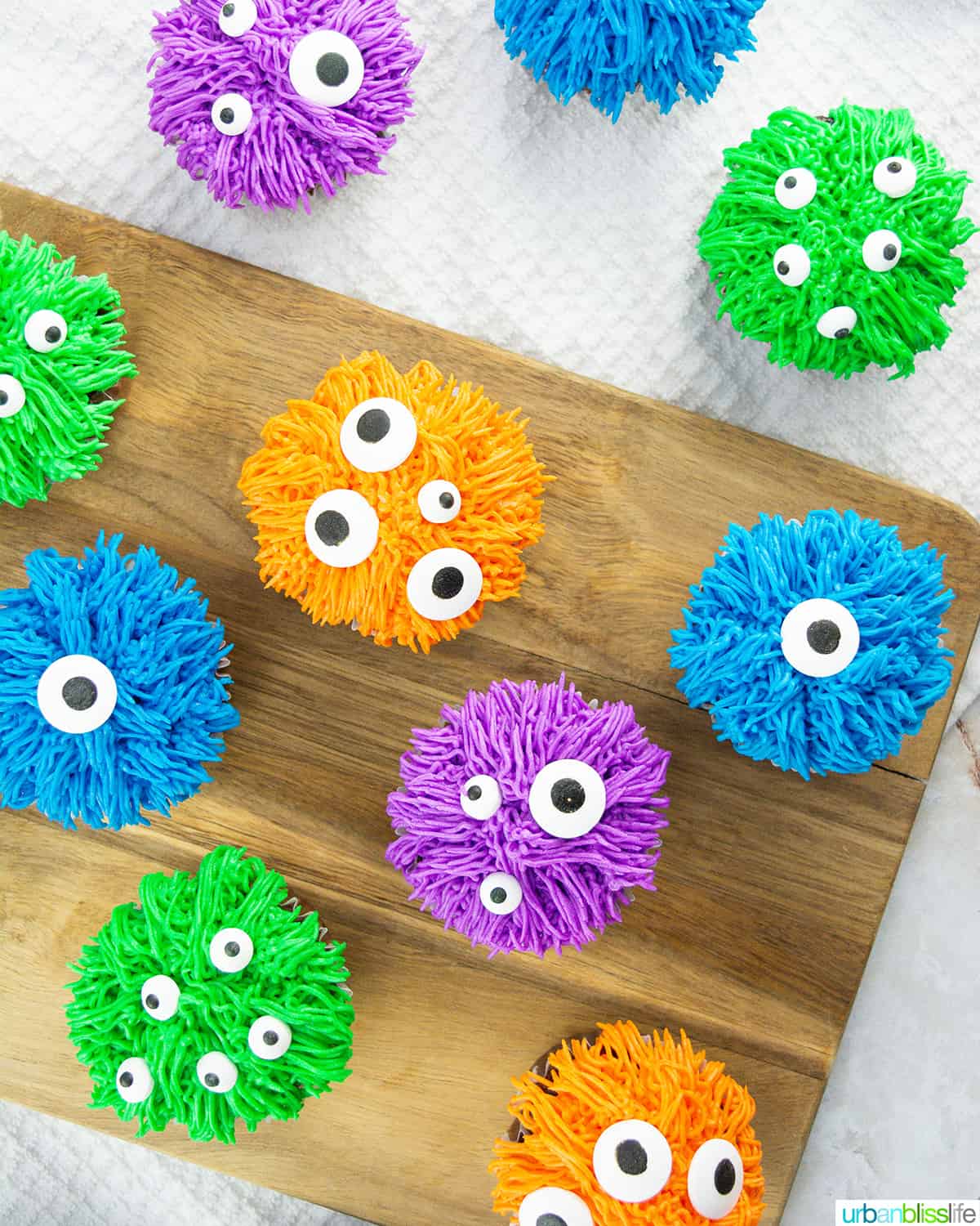 several colorful bright halloween monster cupcakes on a wood board.