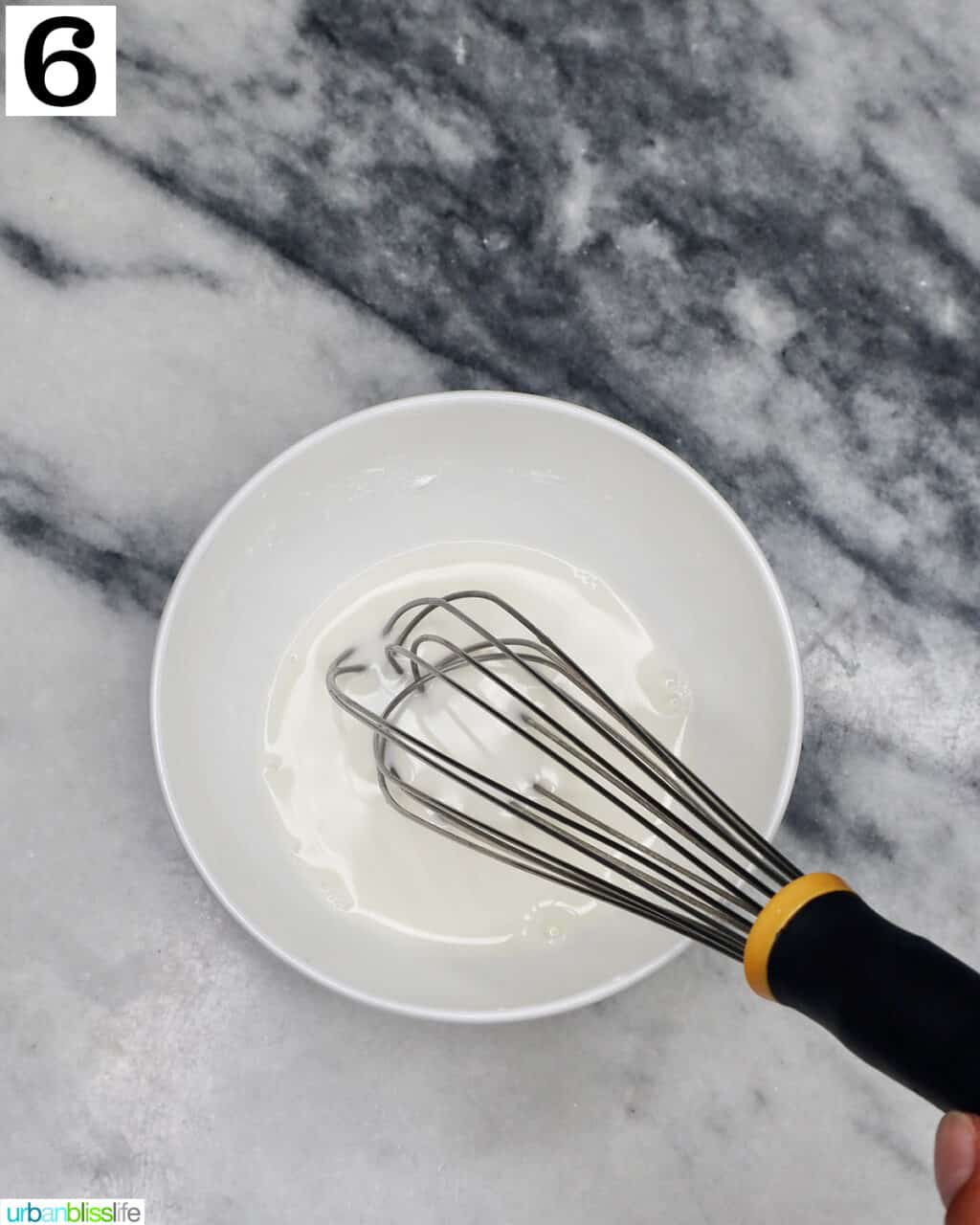 whisk and a white bowl with cornstarch slurry on a marble countertop.