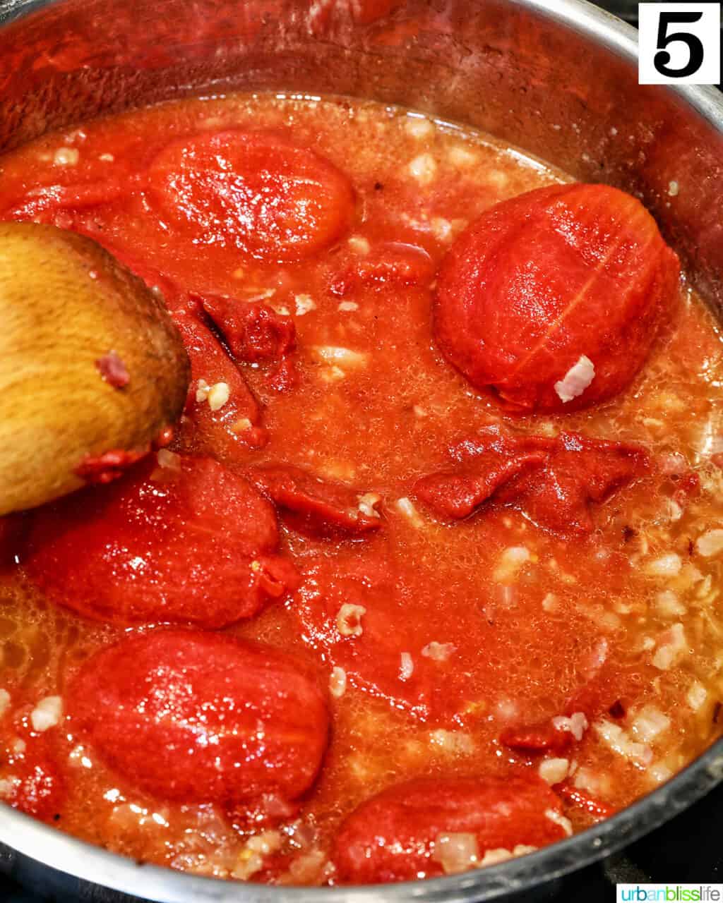 wooden spoon stirring tomatoes in a saucepan.