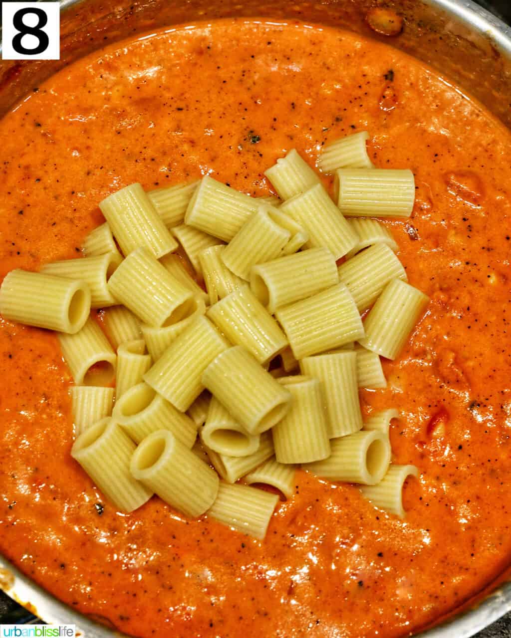 rigatoni added to tomato sauce in a saucepan.