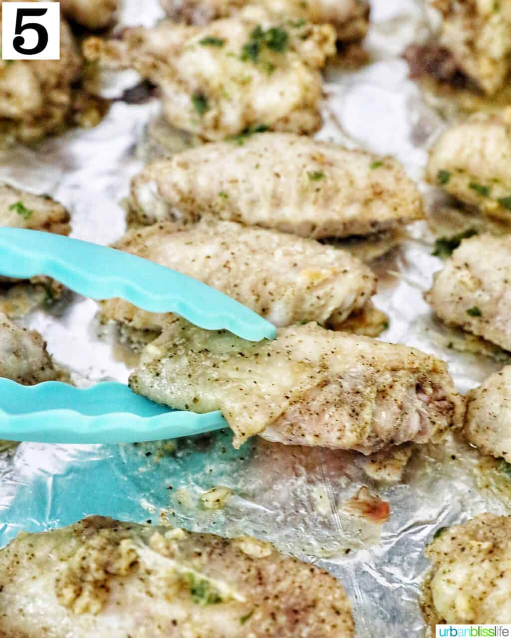 blue tongs turning over a chicken wing on aluminum foil.