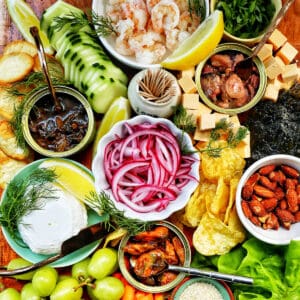 seacuterie board with tinned fish, fruits, vegetables, chips, crackers, and garnishes.