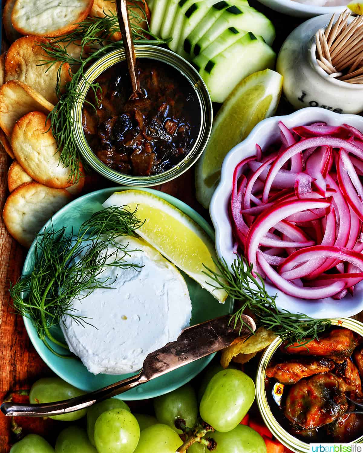 seacuterie board with tinned fish, fruits, vegetables, chips, crackers, and garnishes.