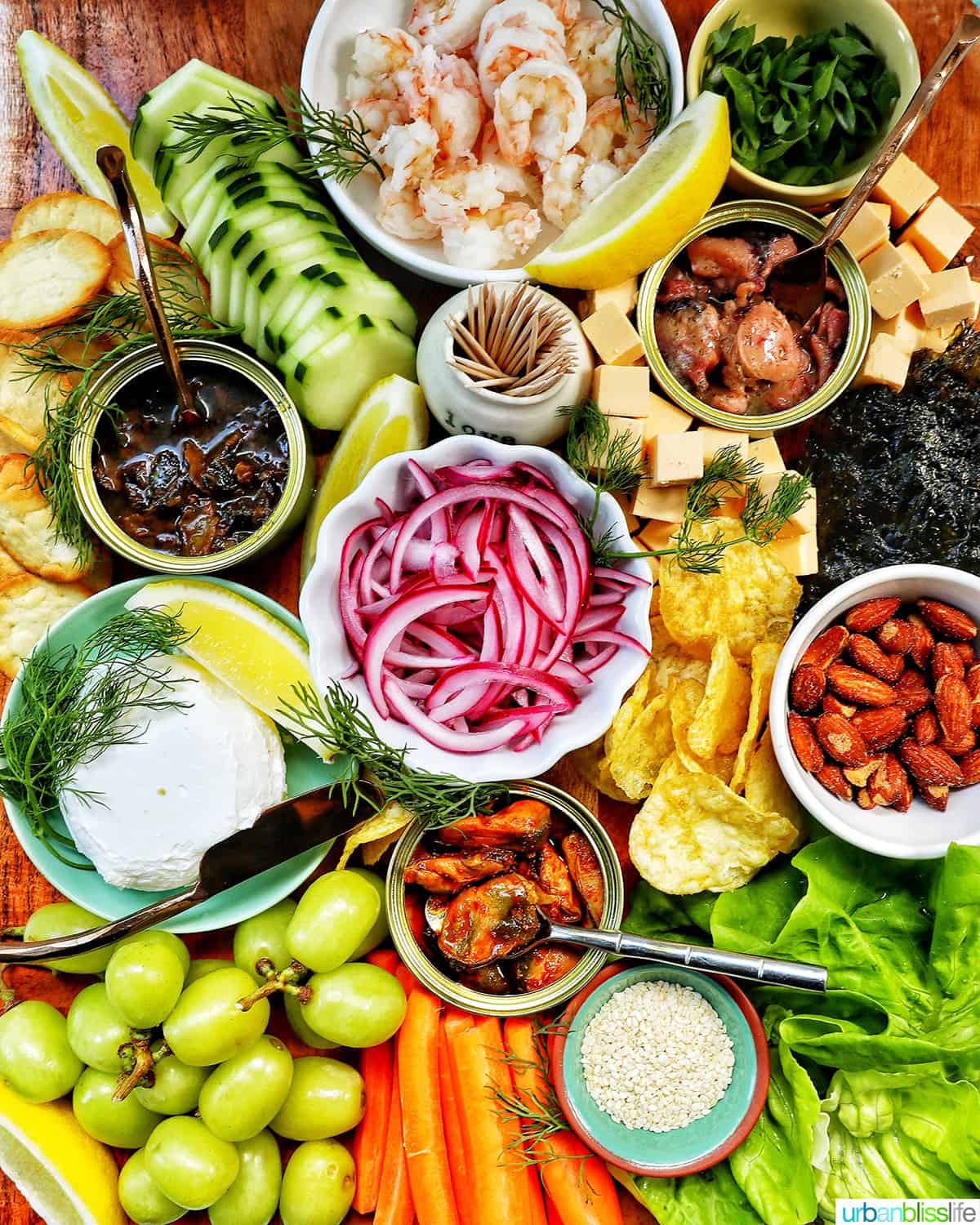 seacuterie board with tinned fish, fruits, vegetables, chips, crackers, and garnishes.