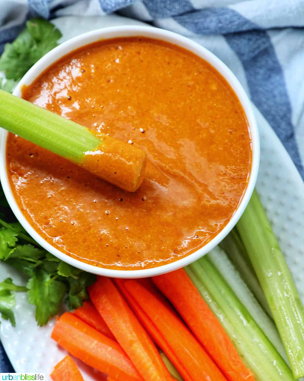 carrot stick dipped into a bowl of vegan buffalo sauce on a plate with carrot and celery sticks and parsley garnish.