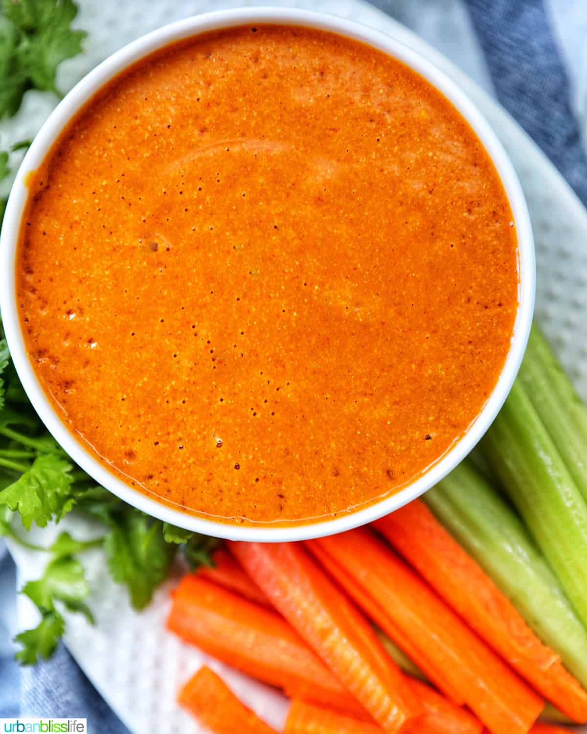 closeup of bowl of vegan buffalo sauce on a plate with carrot and celery sticks and parsley garnish.