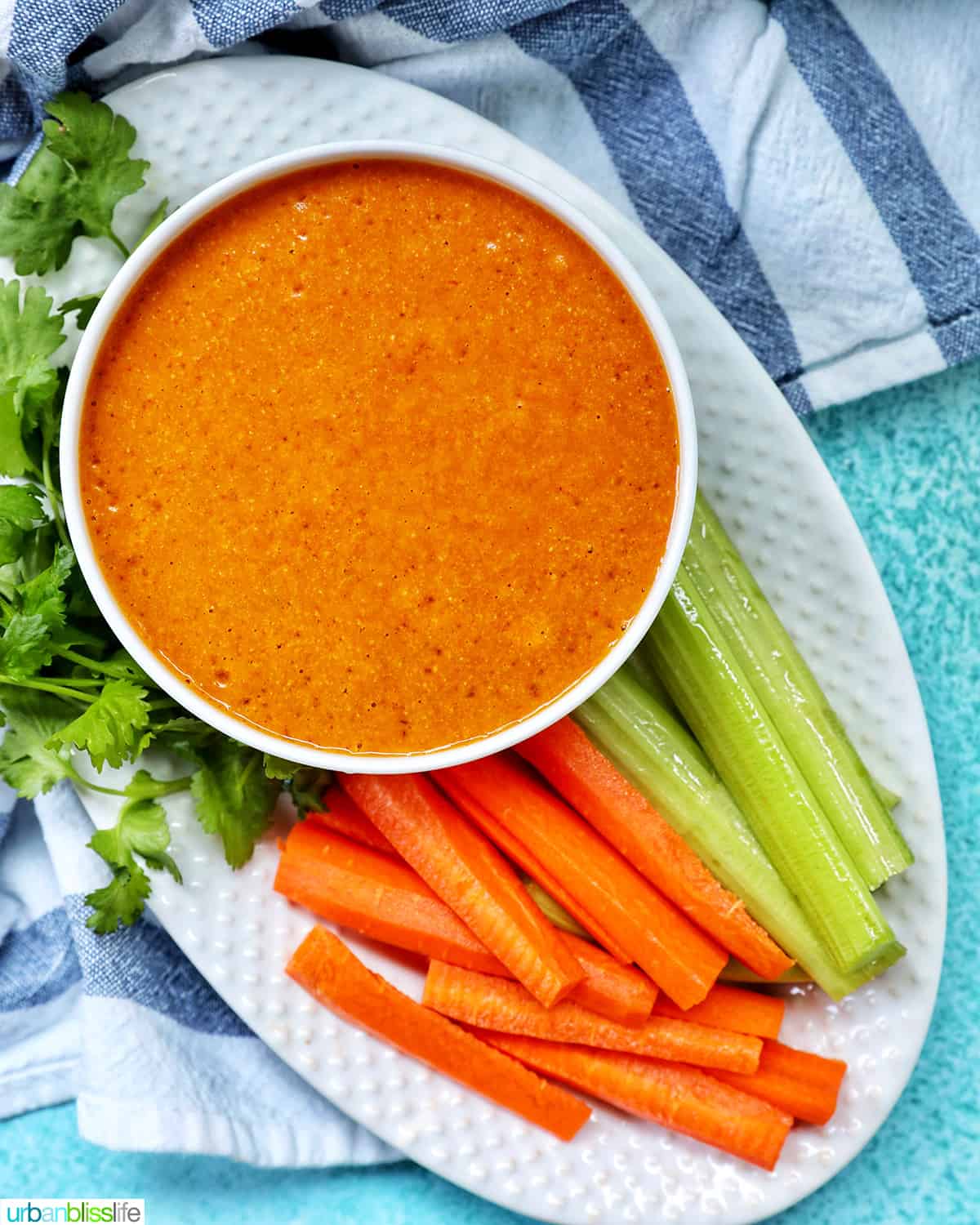 bowl of vegan buffalo sauce on a plate with carrot and celery sticks and parsley garnish.