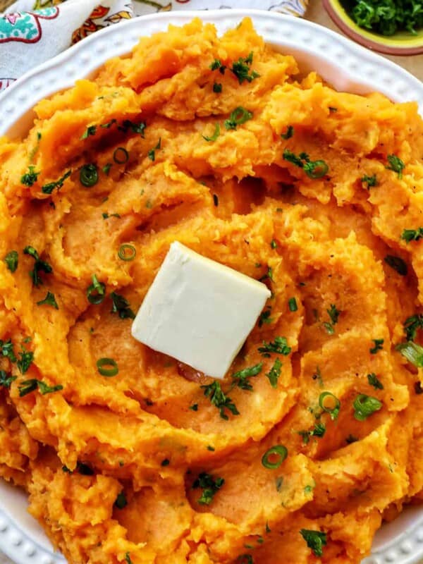 bowl of whipped sweet potatoes and a pat of butter with fresh herbs.