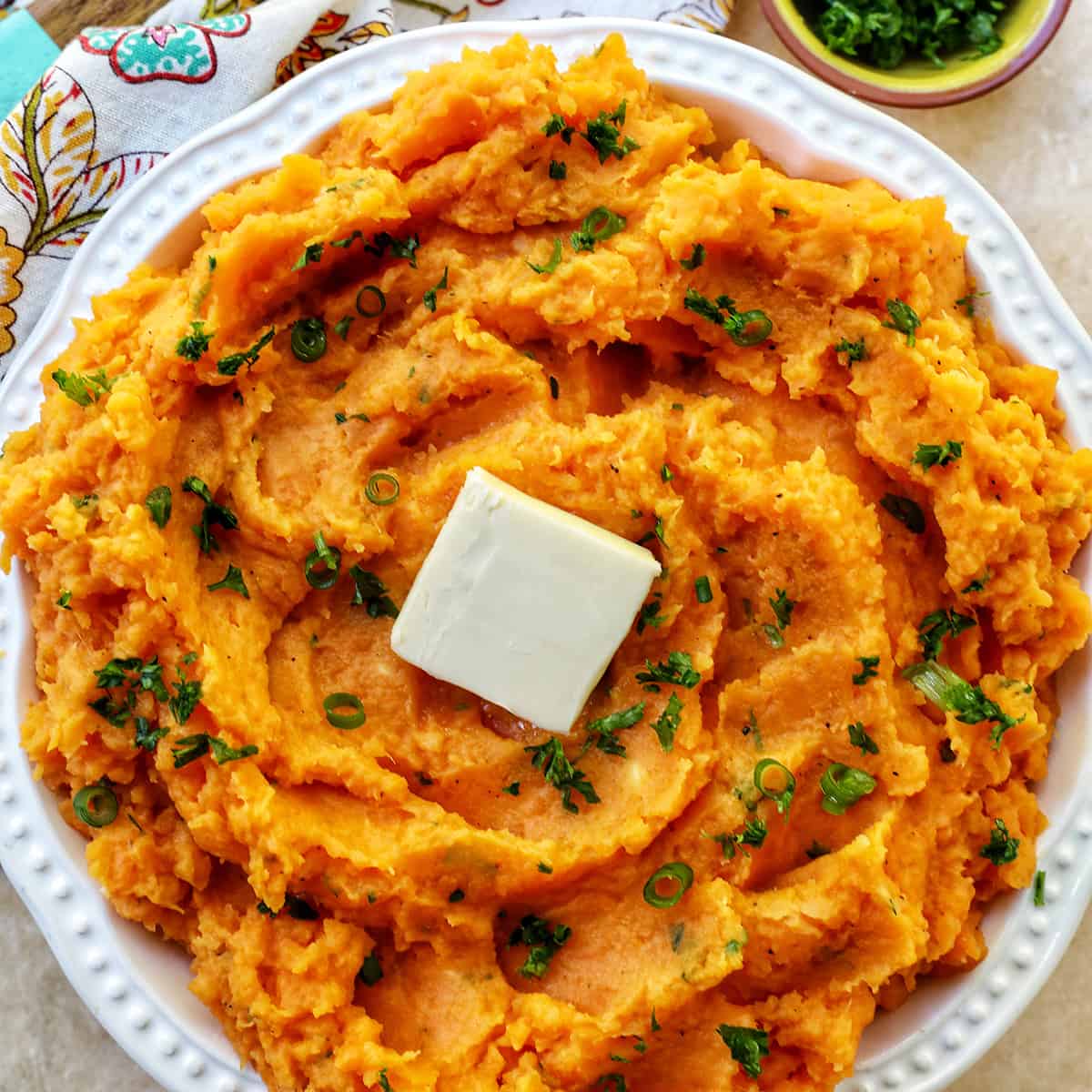 bowl of whipped sweet potatoes and a pat of butter with fresh herbs.