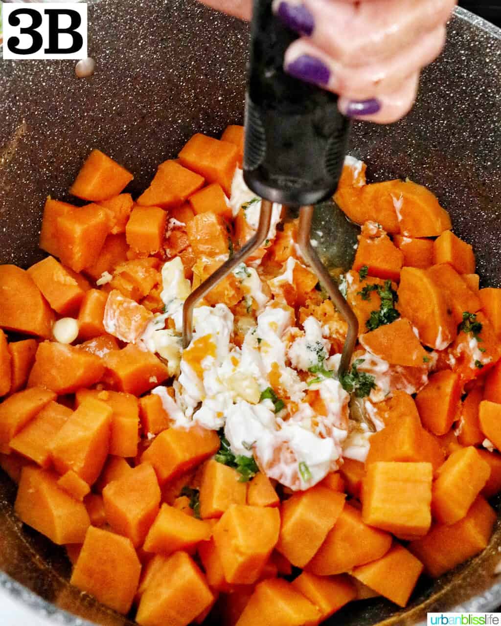 potato masher mashing sour cream, butter, garlic, and herbs into chopped sweet potatoes in a large pot.