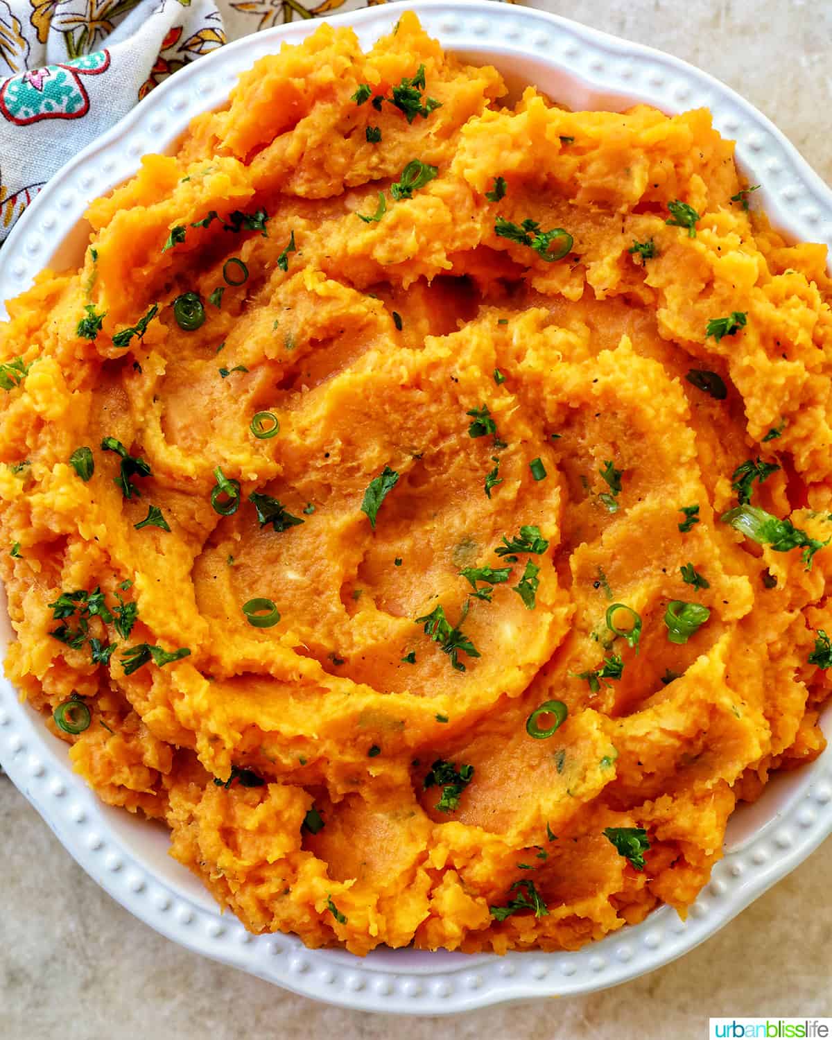 big white bowl full of mashed sweet potatoes and garnished with fresh herbs.