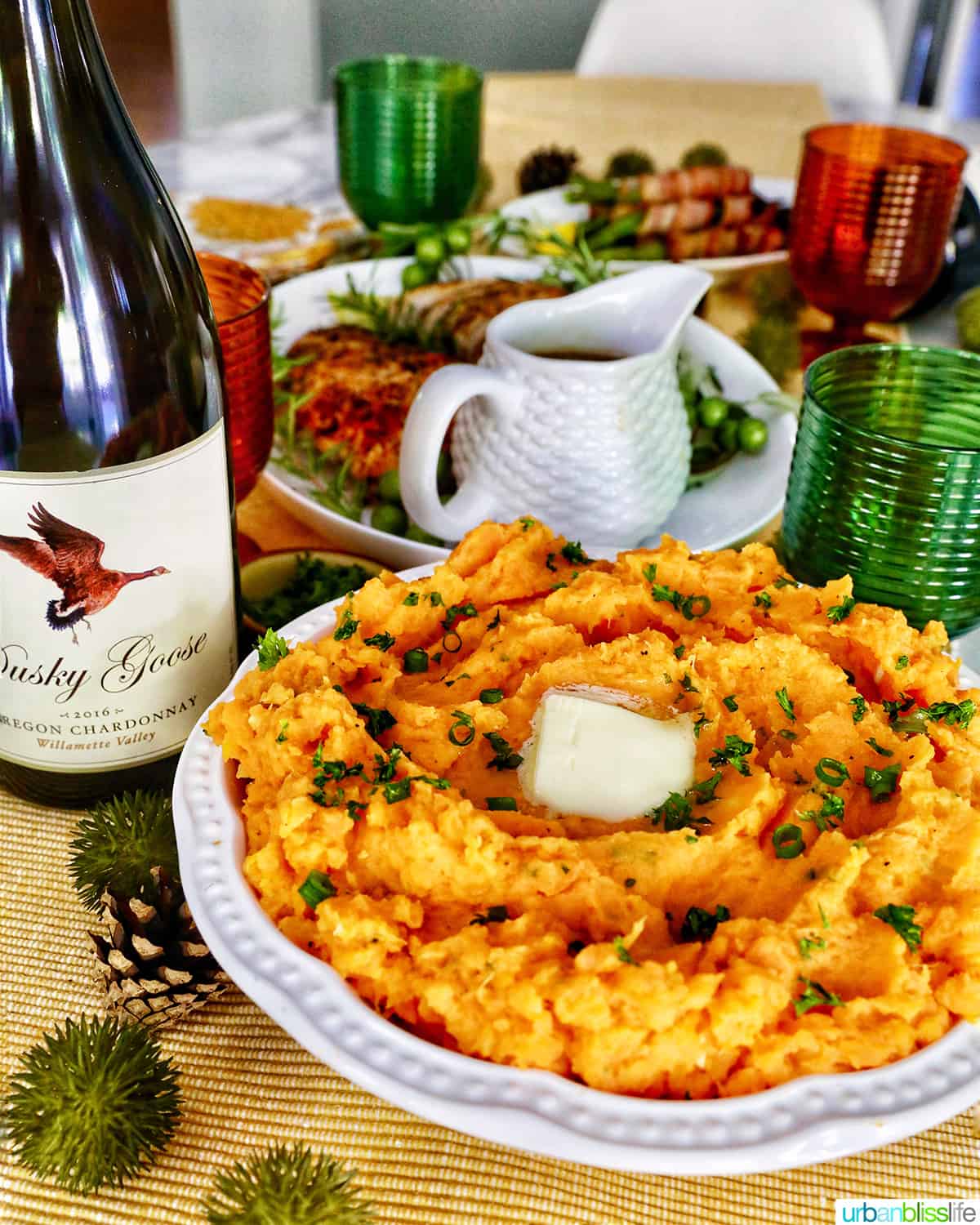 mashed sweet potatoes in a bowl in front of a bottle of dusky goose oregon Chardonnay and a table set for Thanksgiving.