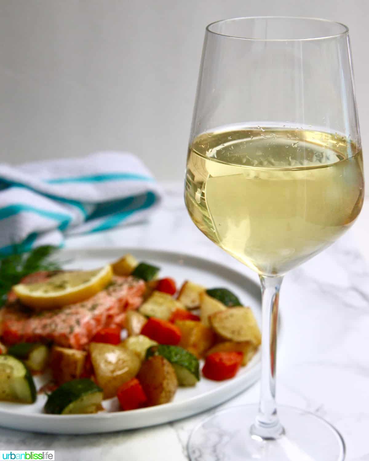 glass of white wine with salmon and vegetables in the background.