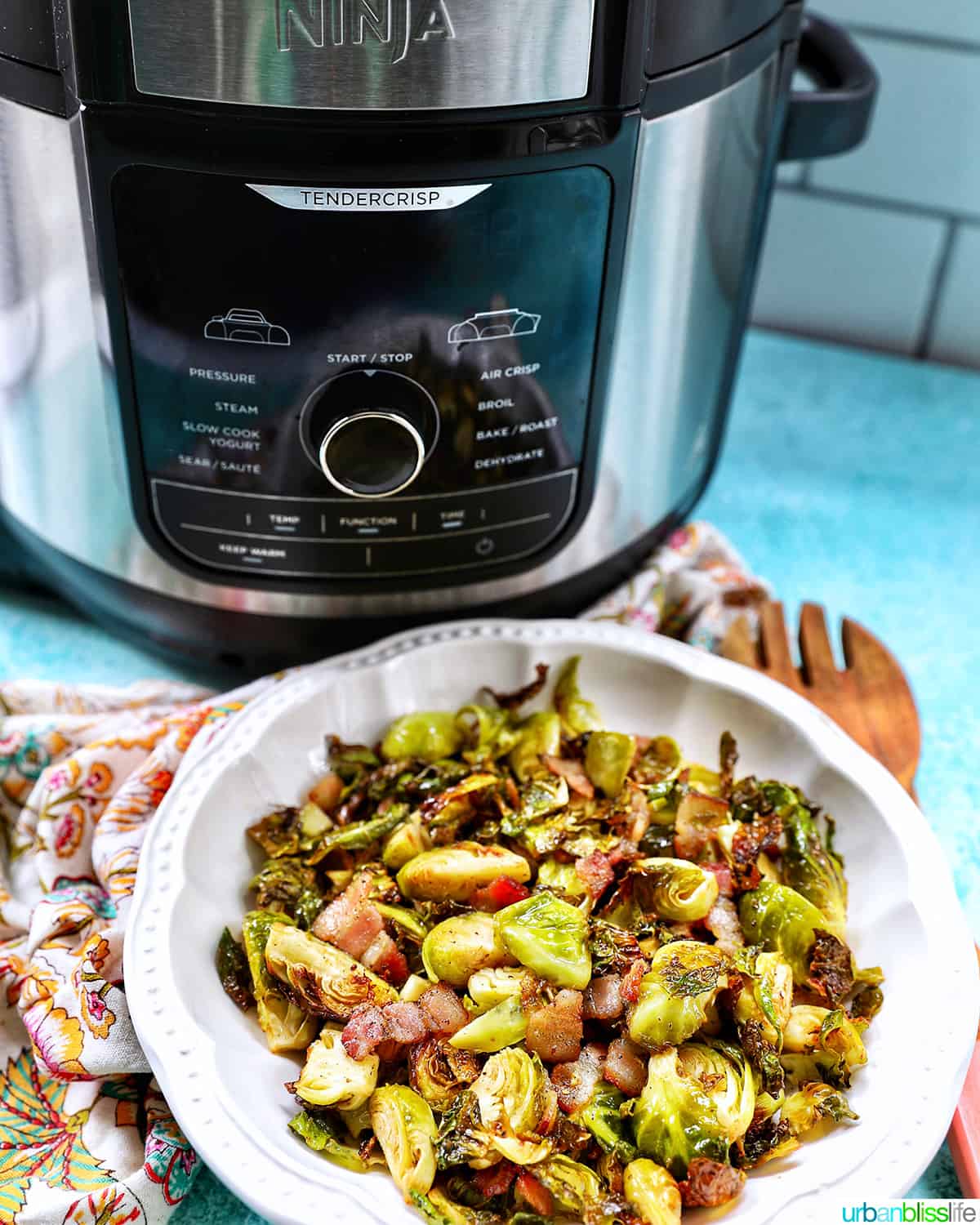 bowl of brussels sprouts with bacon in front of an air fryer.