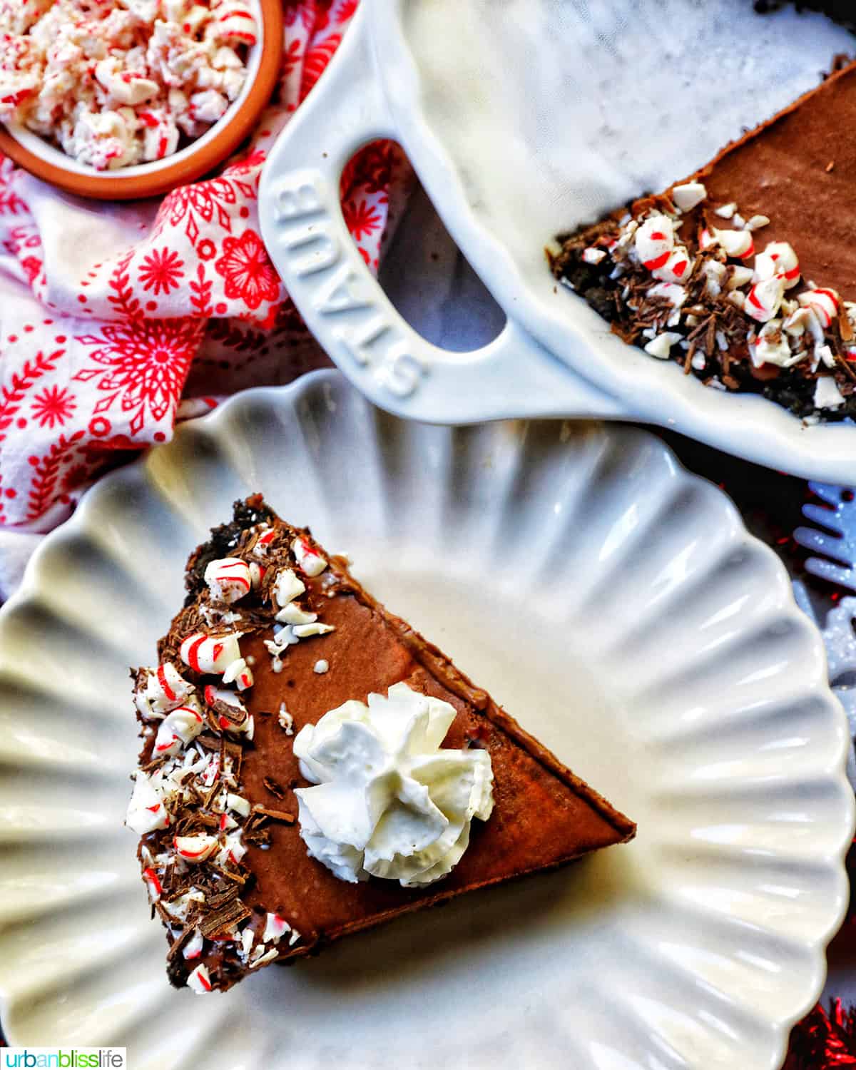 slice of Chocolate Peppermint Pie on a scalloped plate next to the full pie and a bowl of pepperming candies.