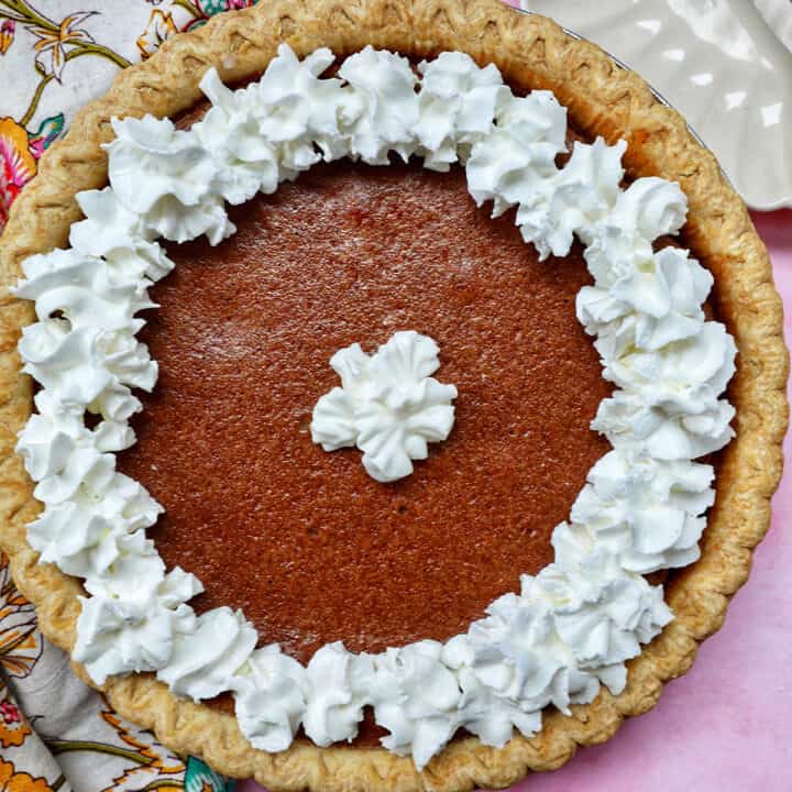 cinnamon pie with whipped cream on a pink background.