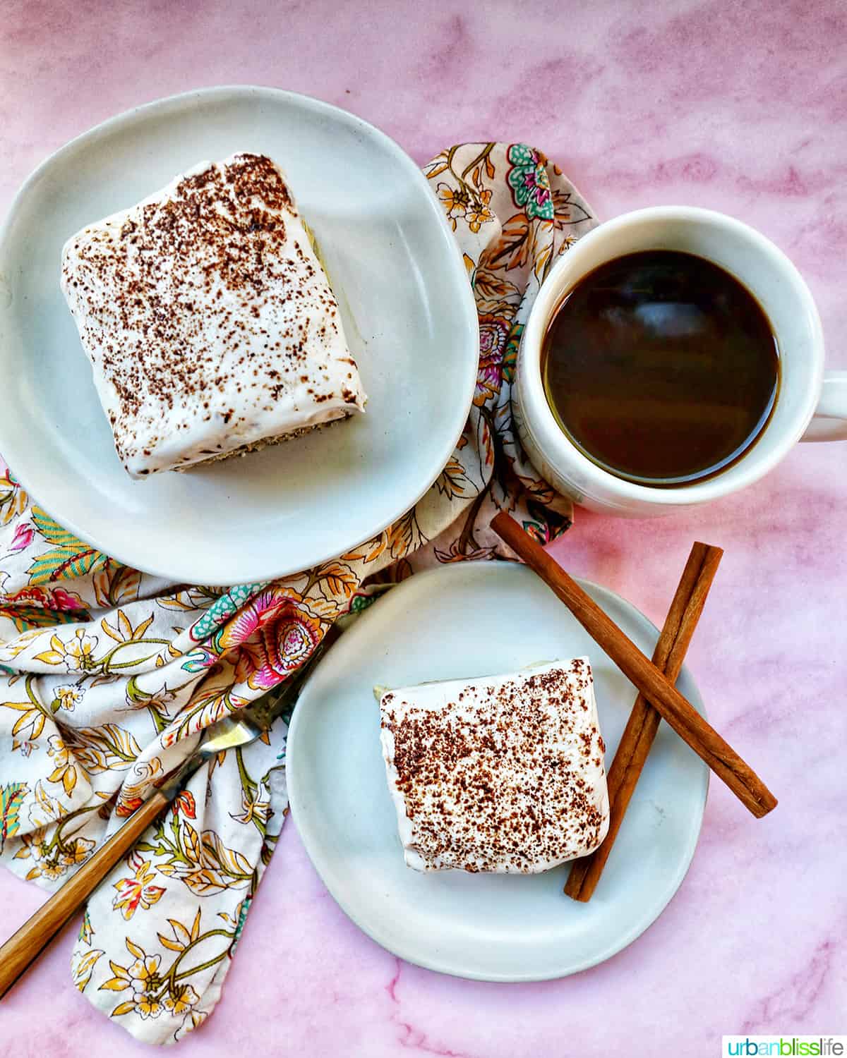 two plates of dairy free tiramisu dessert with a cup of coffee, fork, napkins, and cinnamon sticks.
