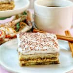 slice of dairy free tiramisu dessert on a white plate with cup of coffee behind it.