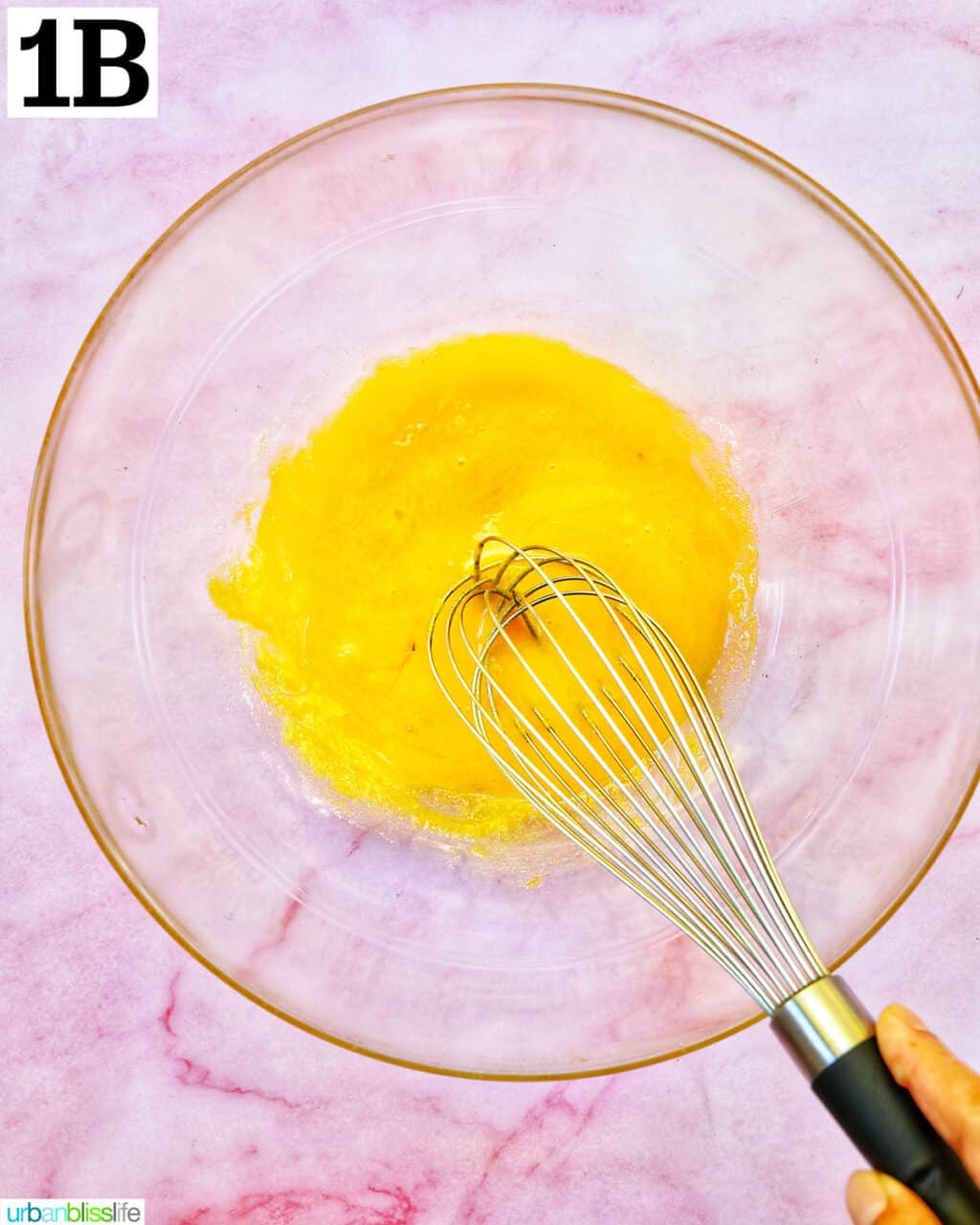 whisk beating egg yolks in a clear glass bowl.