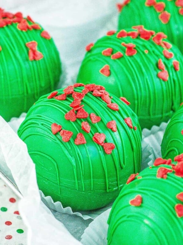 several bright green Grinch hot chocolate bombs with red heart sprinkles.