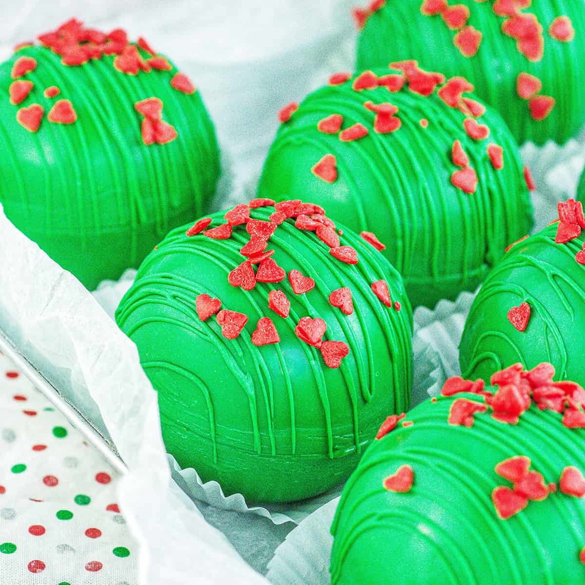 several bright green Grinch hot chocolate bombs with red heart sprinkles.