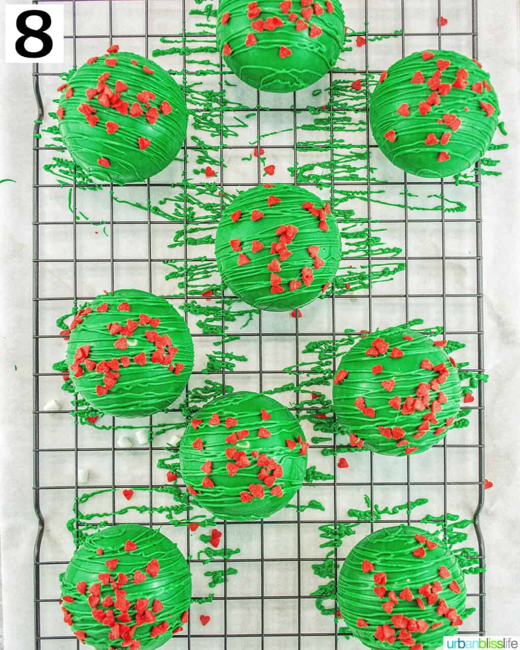 green halves of Grinch hot cocoa bombs with frosting, marshmallows, hot cocoa mix, and red heart sprinkles.