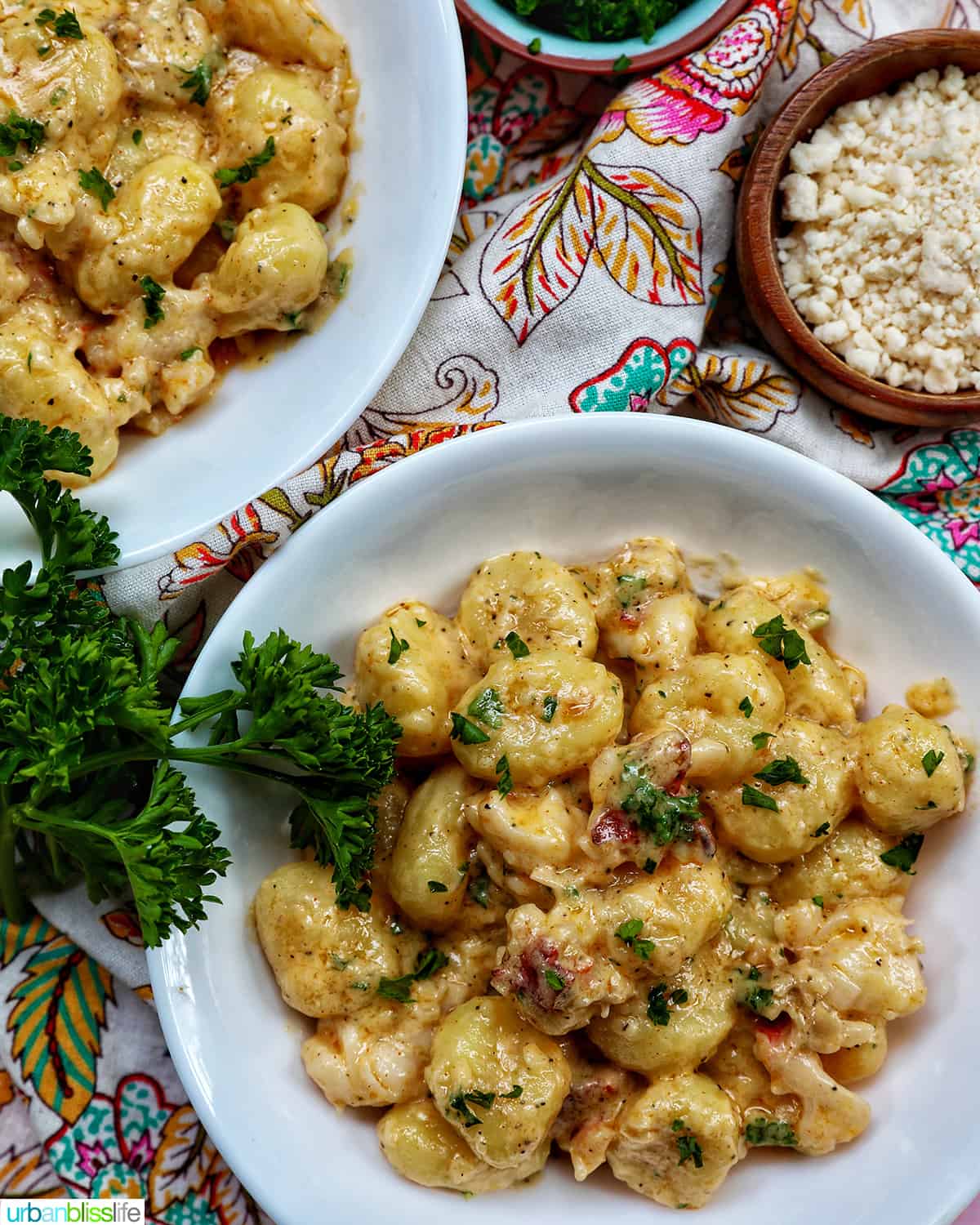 two bowls of lobster gnocchi with herbs and sides of garnishes.